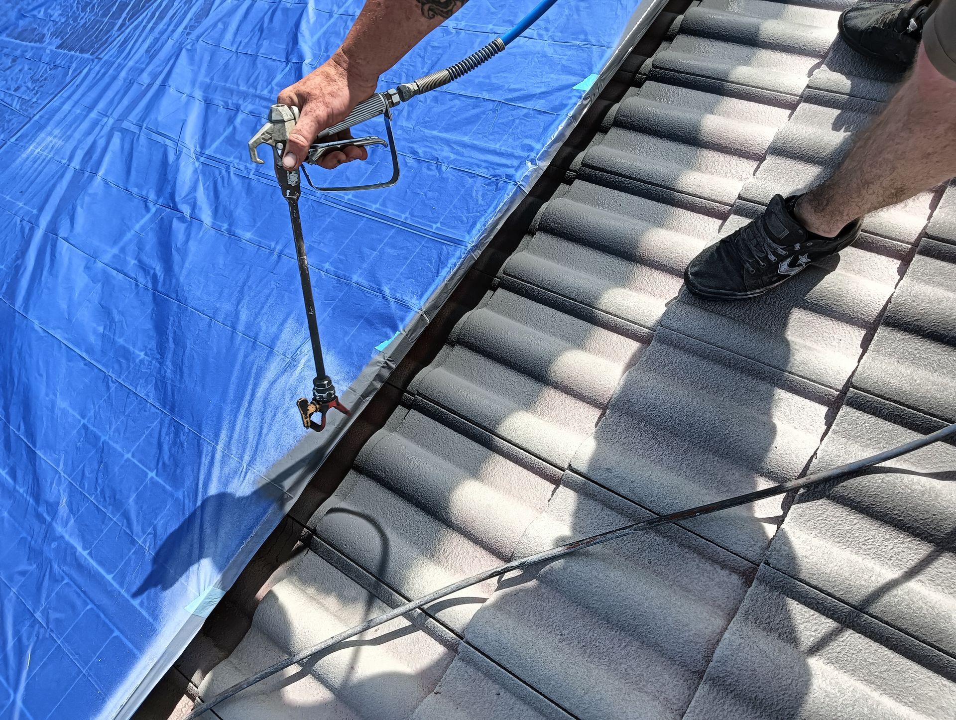 Roof painting in progress with protective coating being spray-applied