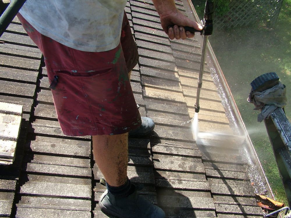 High-pressure washer cleaning moss and grime from a tile roof