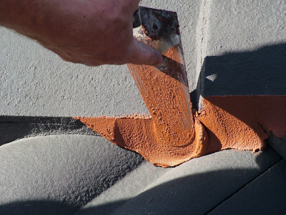 Roofer applying sealant to roof tiles during a roof repair
