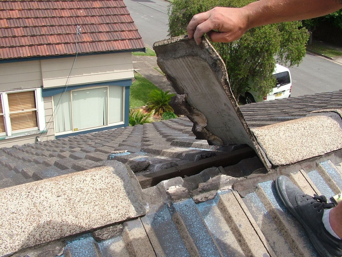 Roofer lifting a cracked concrete tile during a roof repair
