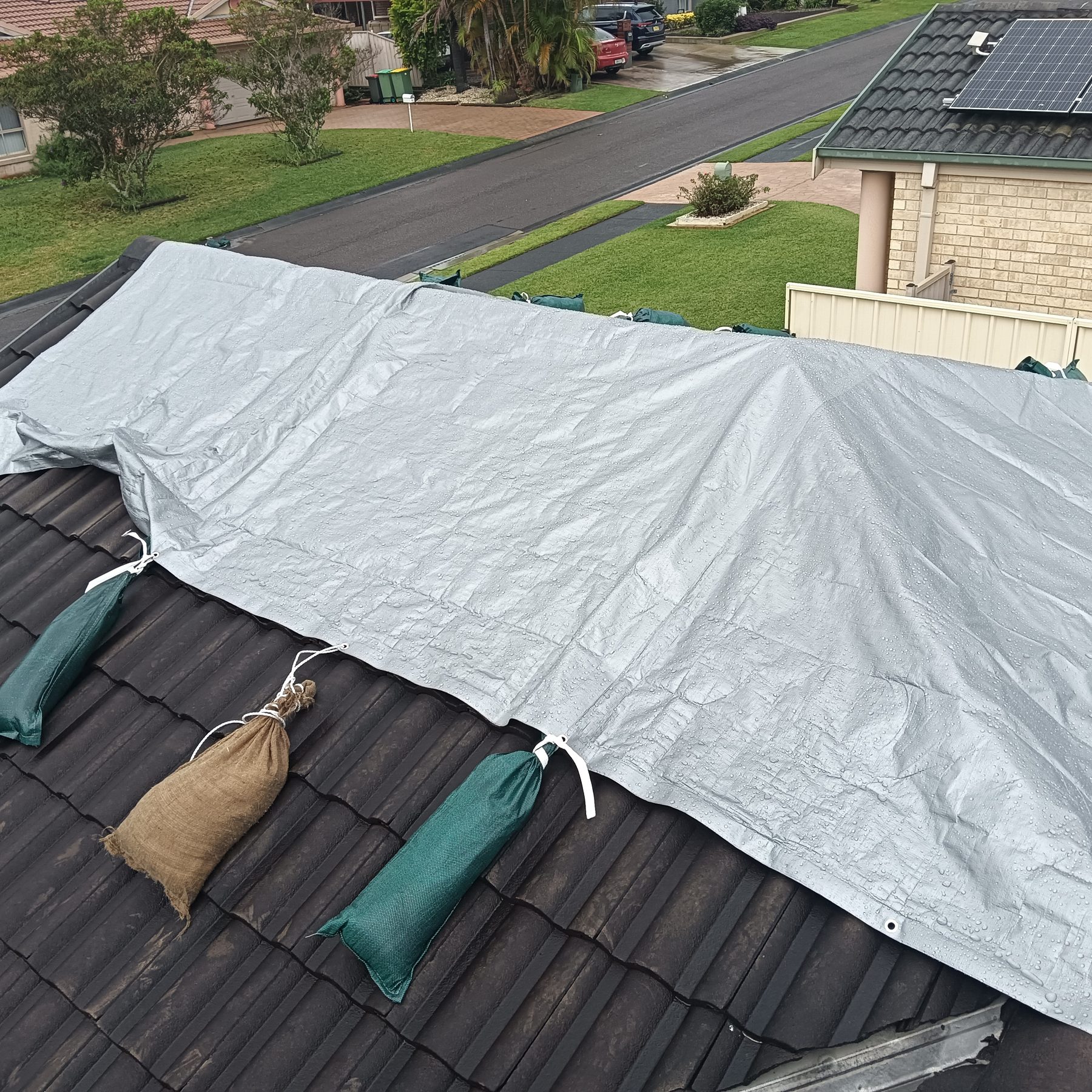 Tarped and sandbagged tile roof on the Central Coast after storm damage and leaks