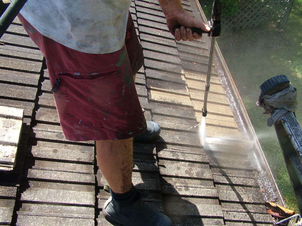 Roof cleaning in progress with a high-pressure washer on a tile roof
