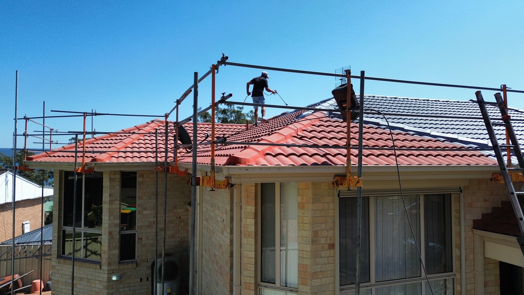 Hunter Valley home mid roof restoration with scaffolding and a roofer coating the tiles